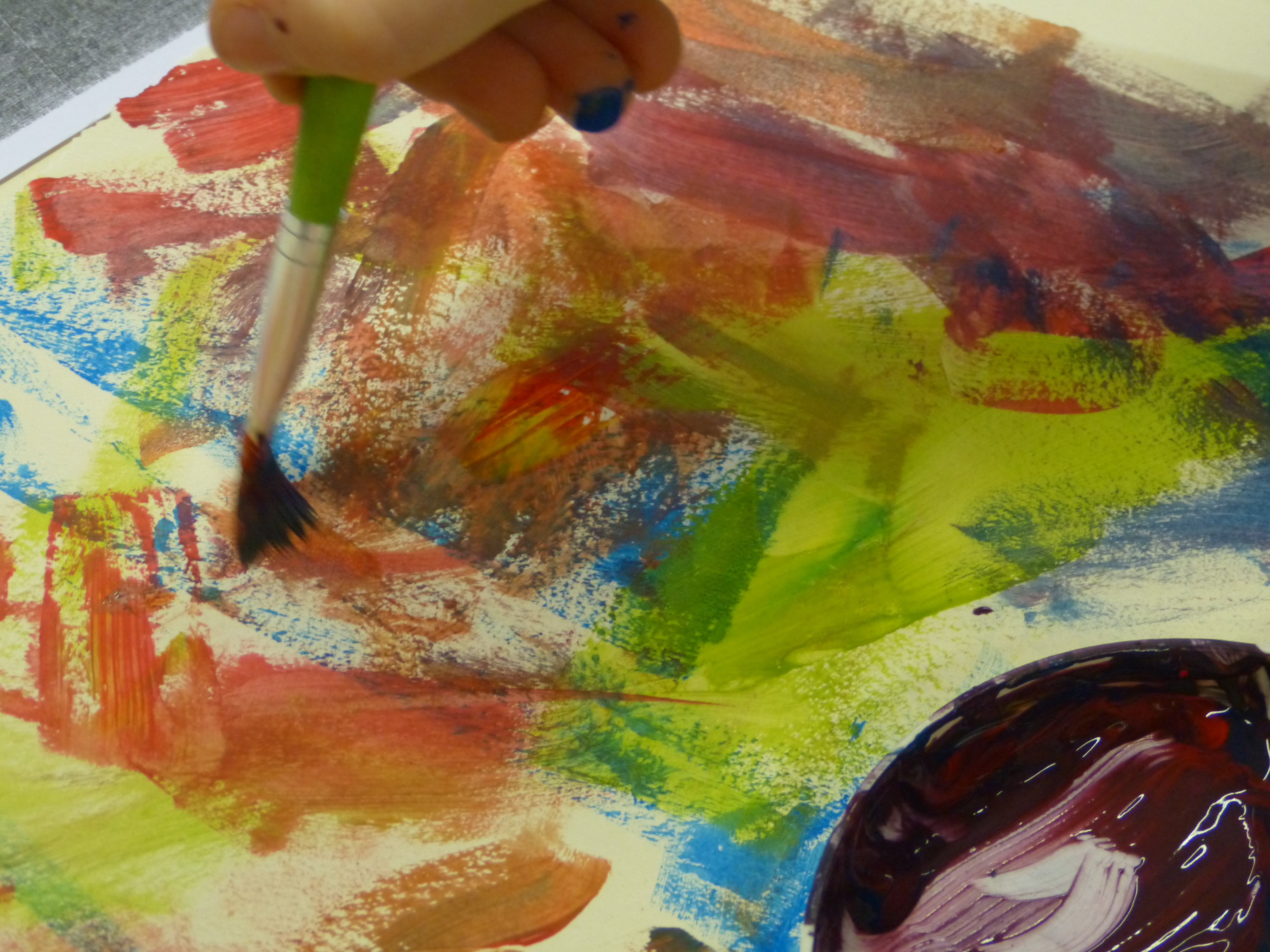 KI generiert: Das Bild zeigt eine Nahaufnahme eines Gemäldes, das in kräftigen Farben wie Blau, Grün, Rot und Gelb gestaltet ist. Eine Hand hält einen Pinsel und malt auf das farbenfrohe Kunstwerk.