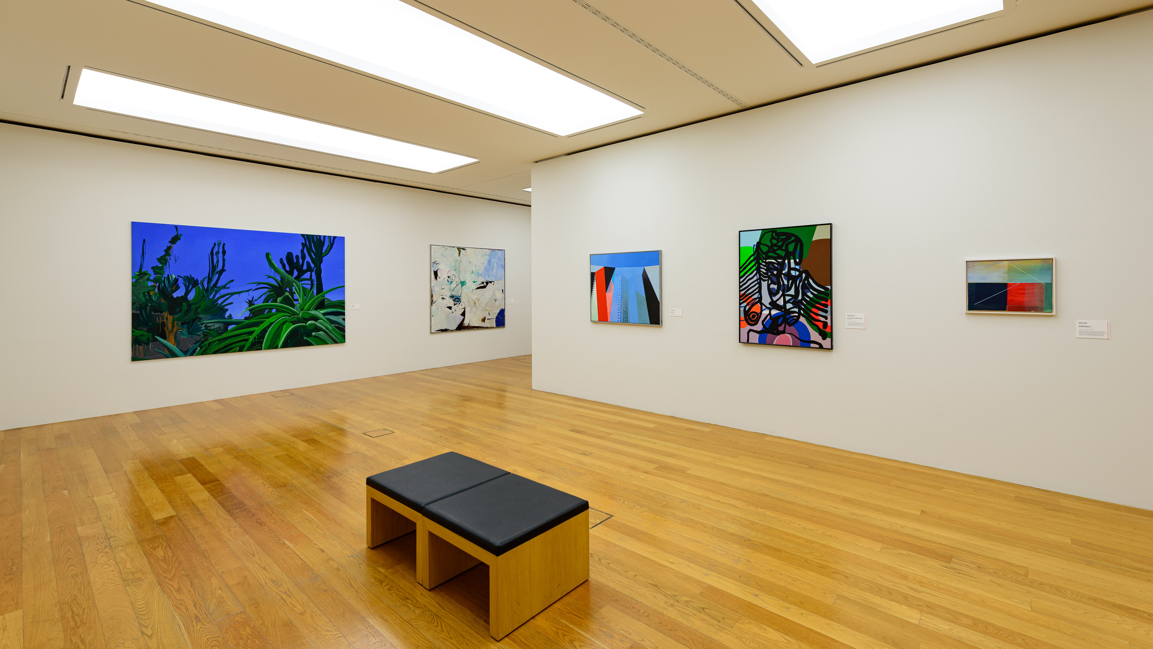 KI generiert: Das Bild zeigt einen modernen Ausstellungsraum in einem Museum oder einer Galerie mit fünf farbenfrohen Gemälden, die an den Wänden hängen. In der Mitte des Raums steht eine einfache Sitzbank auf einem Holzfußboden.