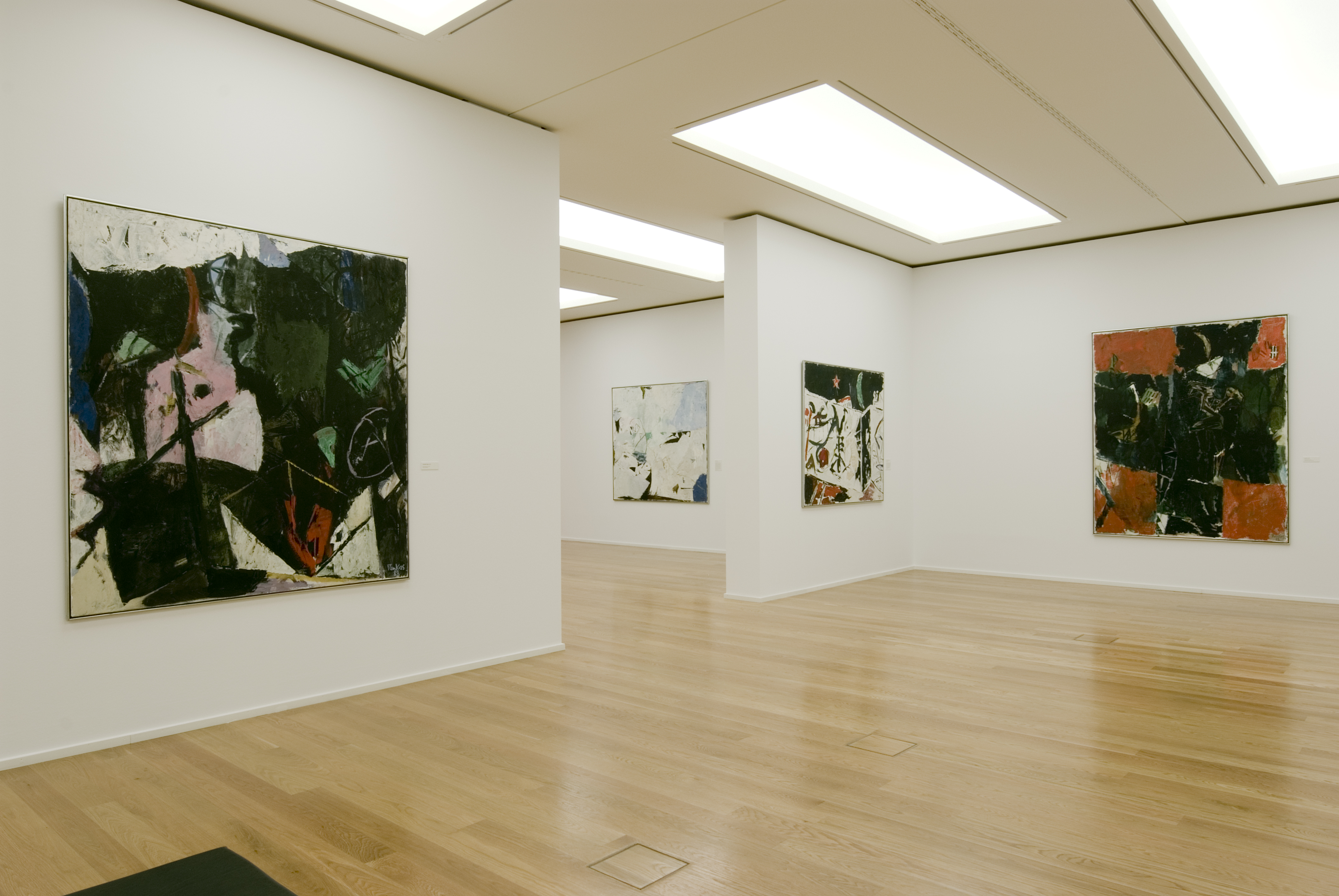 KI generiert: Das Bild zeigt eine moderne Kunstgalerie mit abstrakten Gemälden an den weißen Wänden. Der Raum hat einen hölzernen Boden und ist von einer klaren, minimalistischen Architektur geprägt.