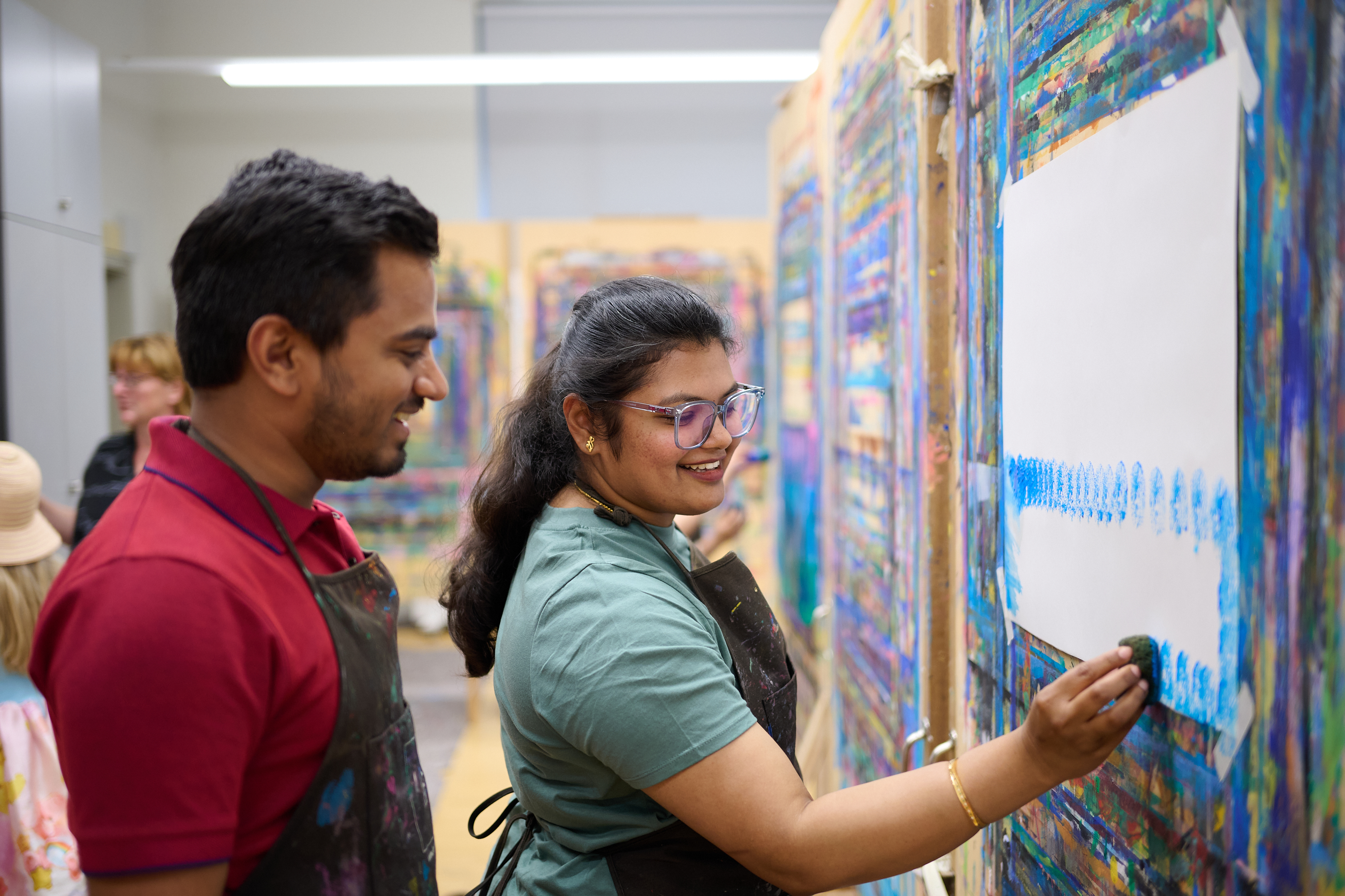 AI generated: The image shows two people painting in a studio. One person is applying paint to a canvas while the other looks on with interest.
