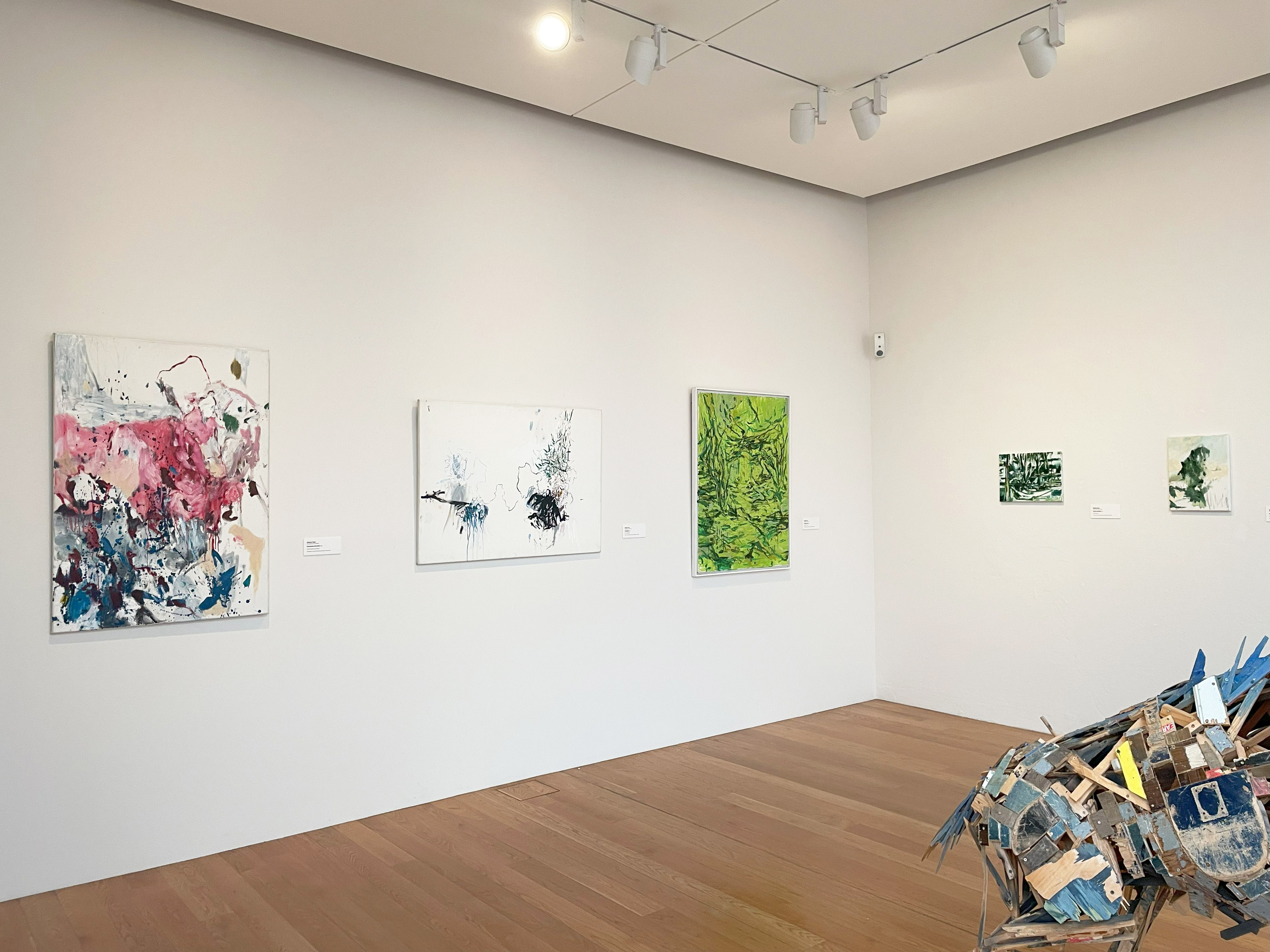 AI generated: The image shows a gallery with several abstract paintings on the wall in different colours. On the floor is a sculptural installation made of wood and leftover paint.