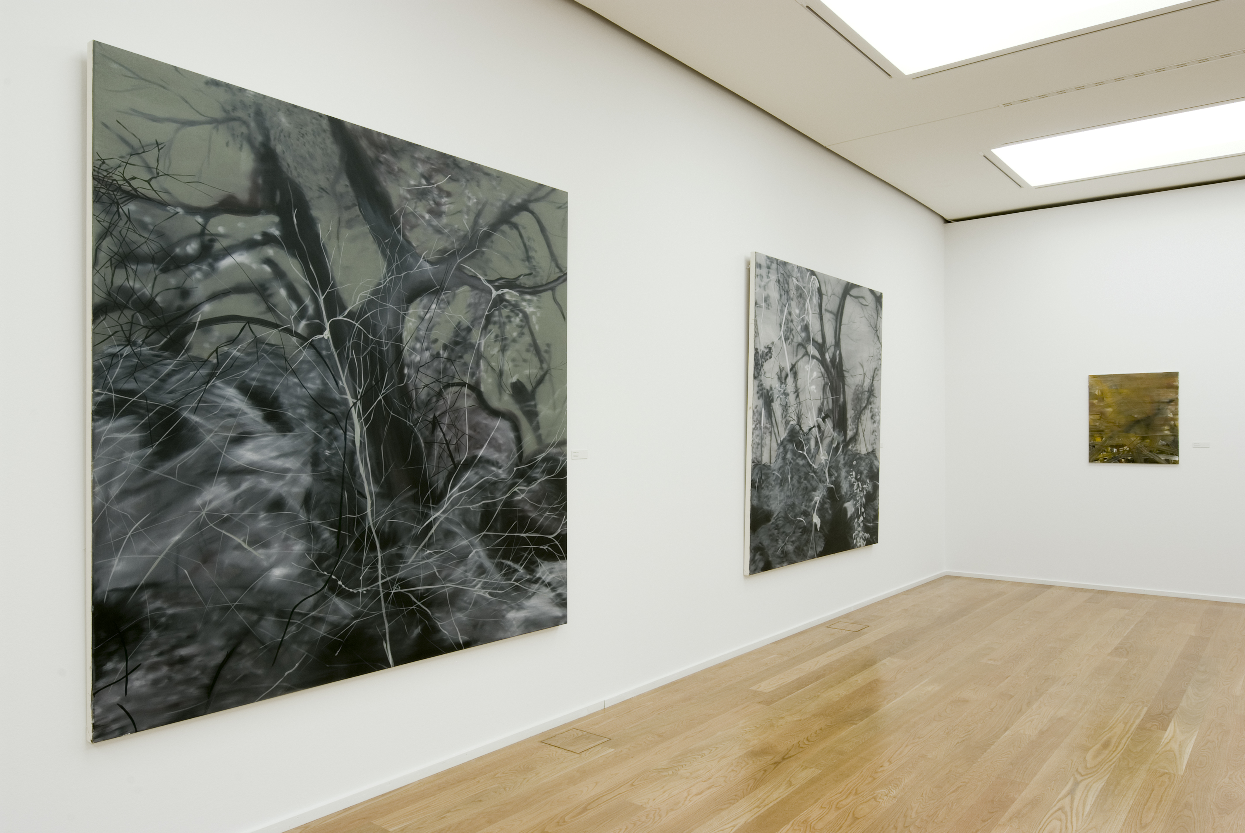 KI generiert: Das Bild zeigt eine Galerie mit mehreren großformatigen Kunstwerken an den Wänden, die abstrahierte Darstellungen von Bäumen oder Waldszenen zeigen. Der Raum hat einen Holzboden und ist hell beleuchtet.