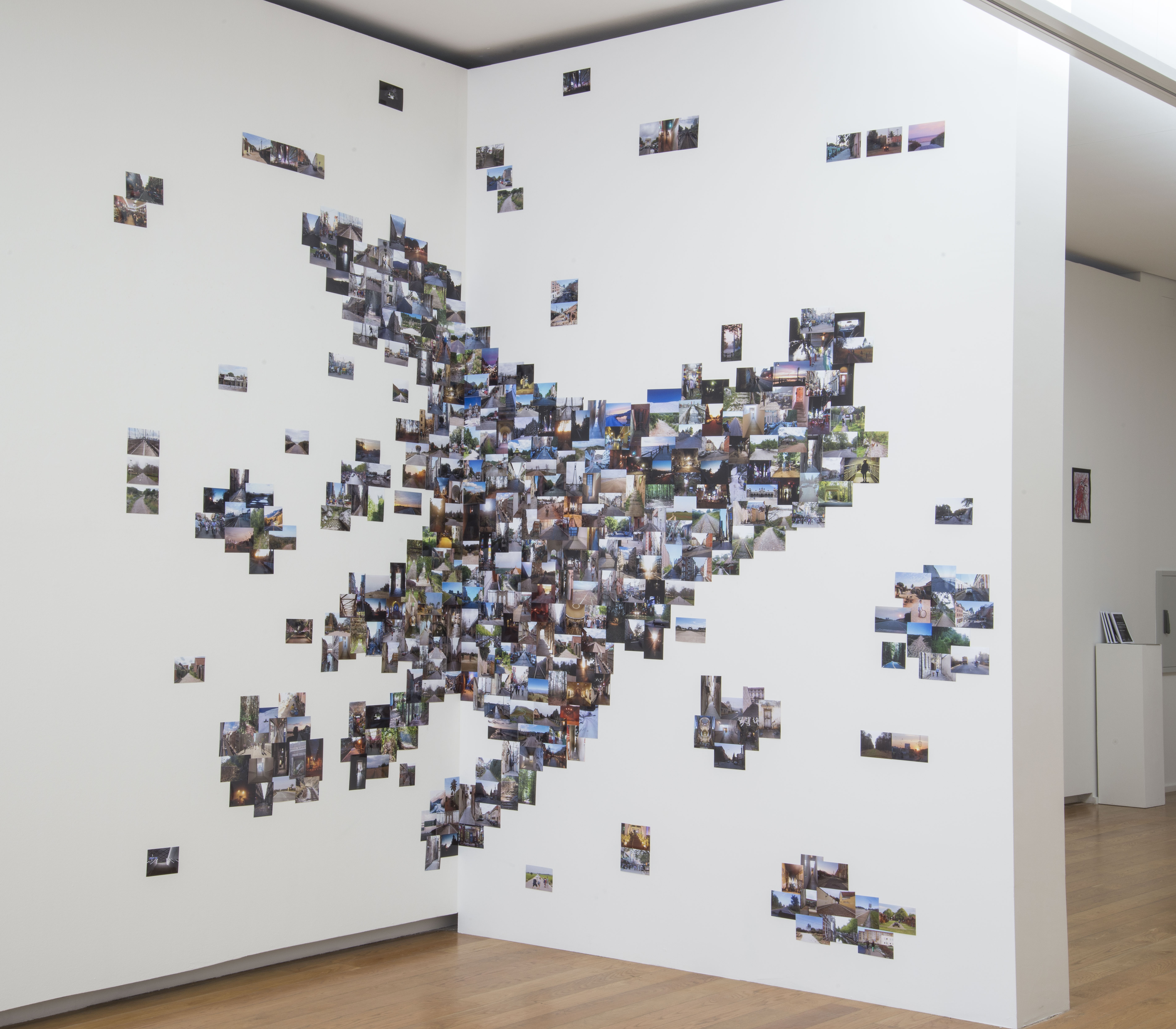 AI generated: The image shows a wall installation consisting of numerous small photos placed close together on a white wall, forming a kind of broad, organic pattern. This image composition gives the impression of an artistic photo collection or collage.