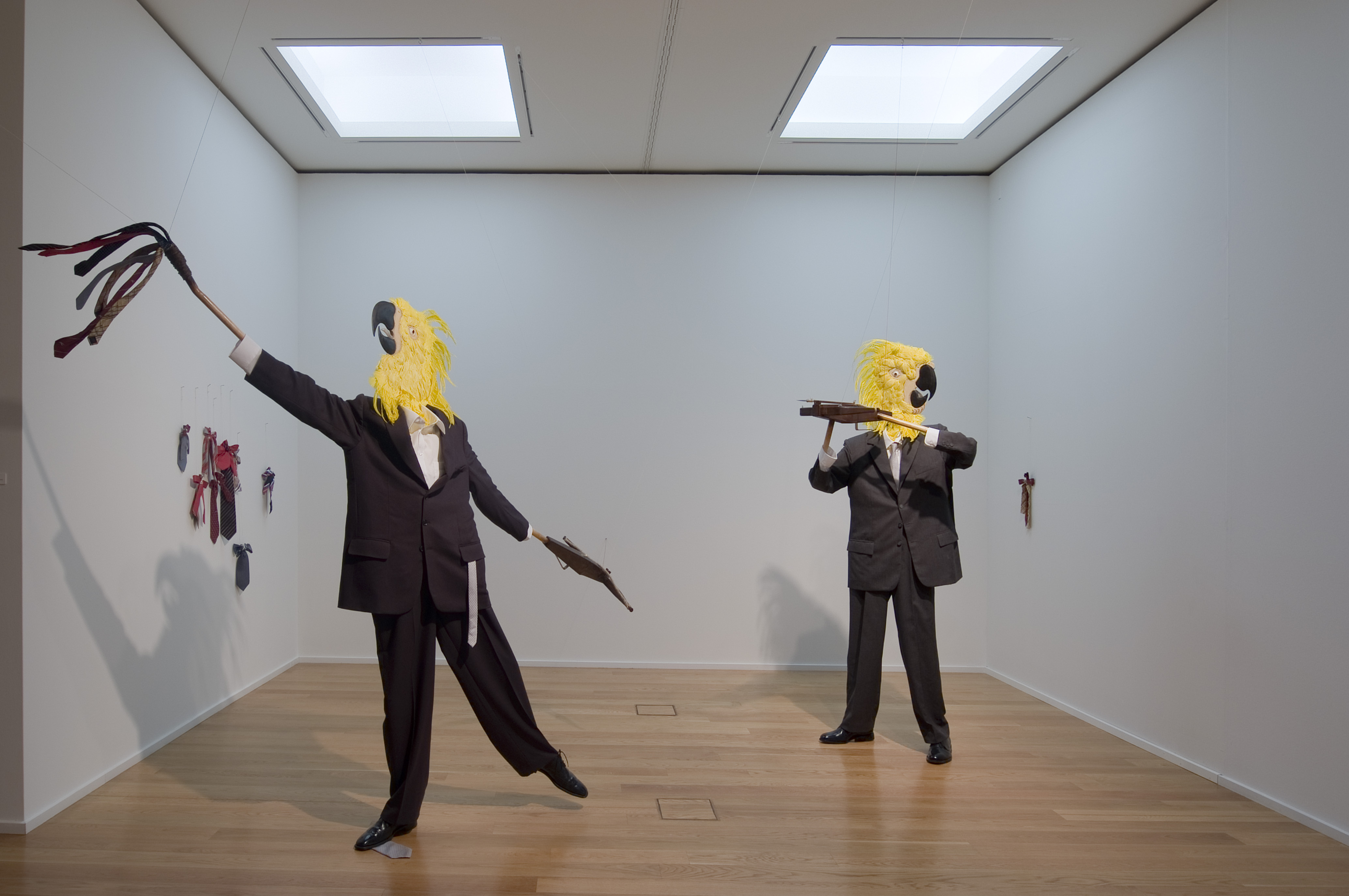 AI generated: The image shows an artistic installation with two figures in suits and yellow bird masks standing in a white room. The figures are holding unusual objects in their hands that resemble an artistic performance or representation.