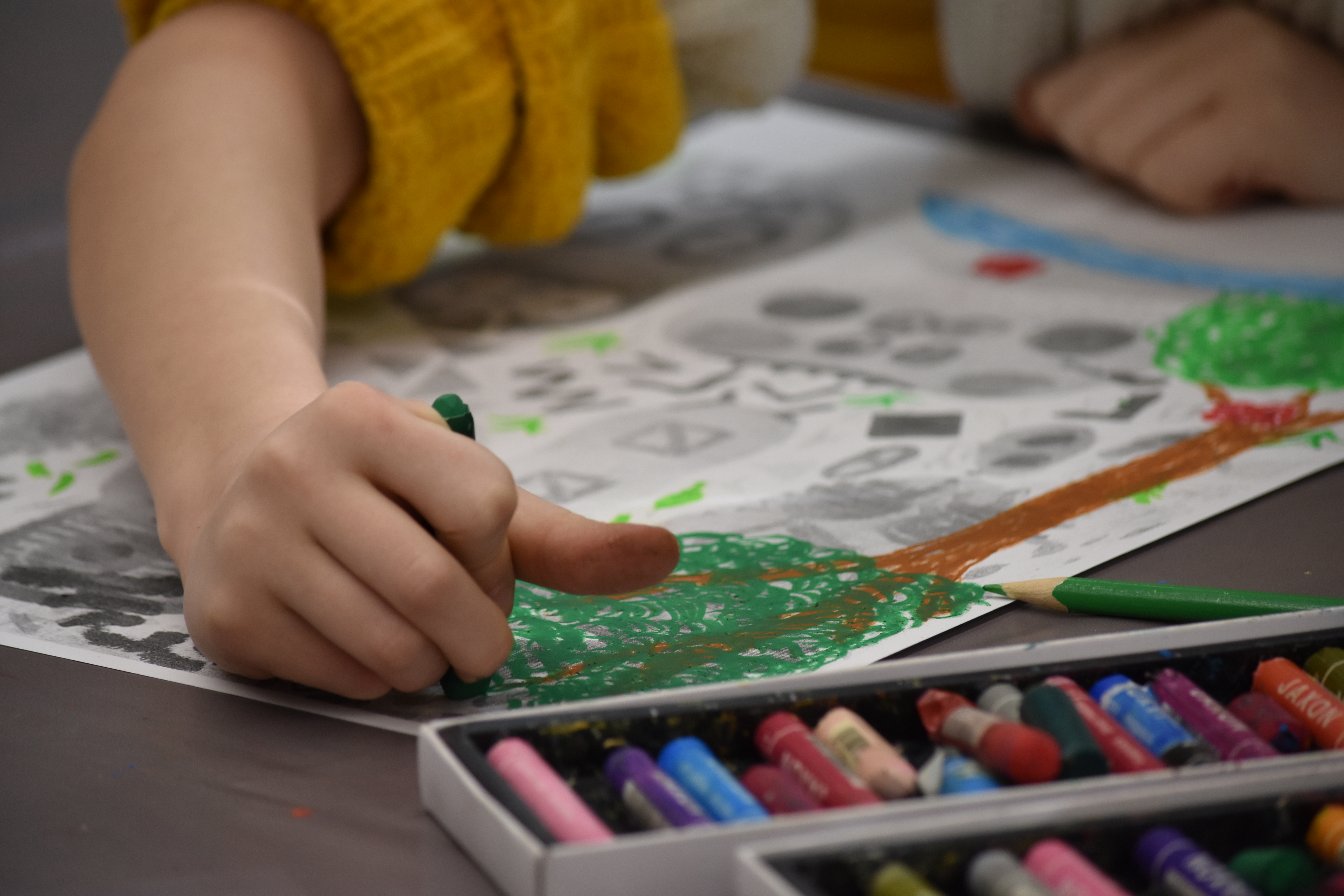 KI generiert: Ein Kind in rotem Pullover arbeitet mit seinen Händen an einem bunten Kunstwerk auf Papier. Der Fokus liegt auf den Händen und dem teilweise fertigen Bild.