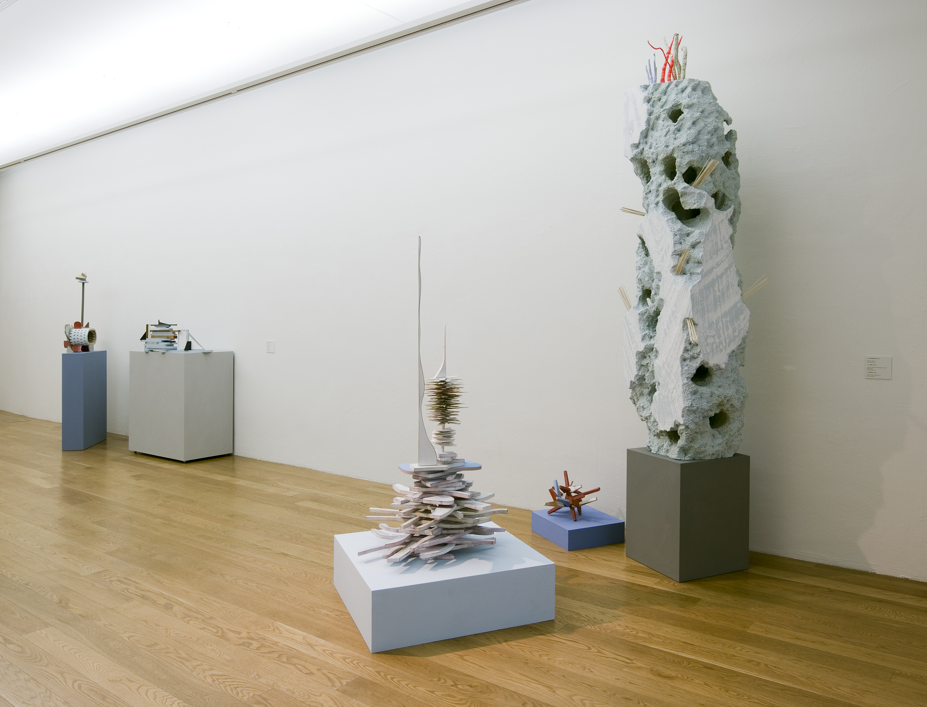 KI generiert: Das Bild zeigt eine Galerieausstellung mit mehreren abstrakten Skulpturen, die jeweils auf eigenen Sockeln platziert sind. Die Kunstwerke variieren in Form und Material und sind in einem minimalistischen Raum mit Holzfußboden präsentiert.