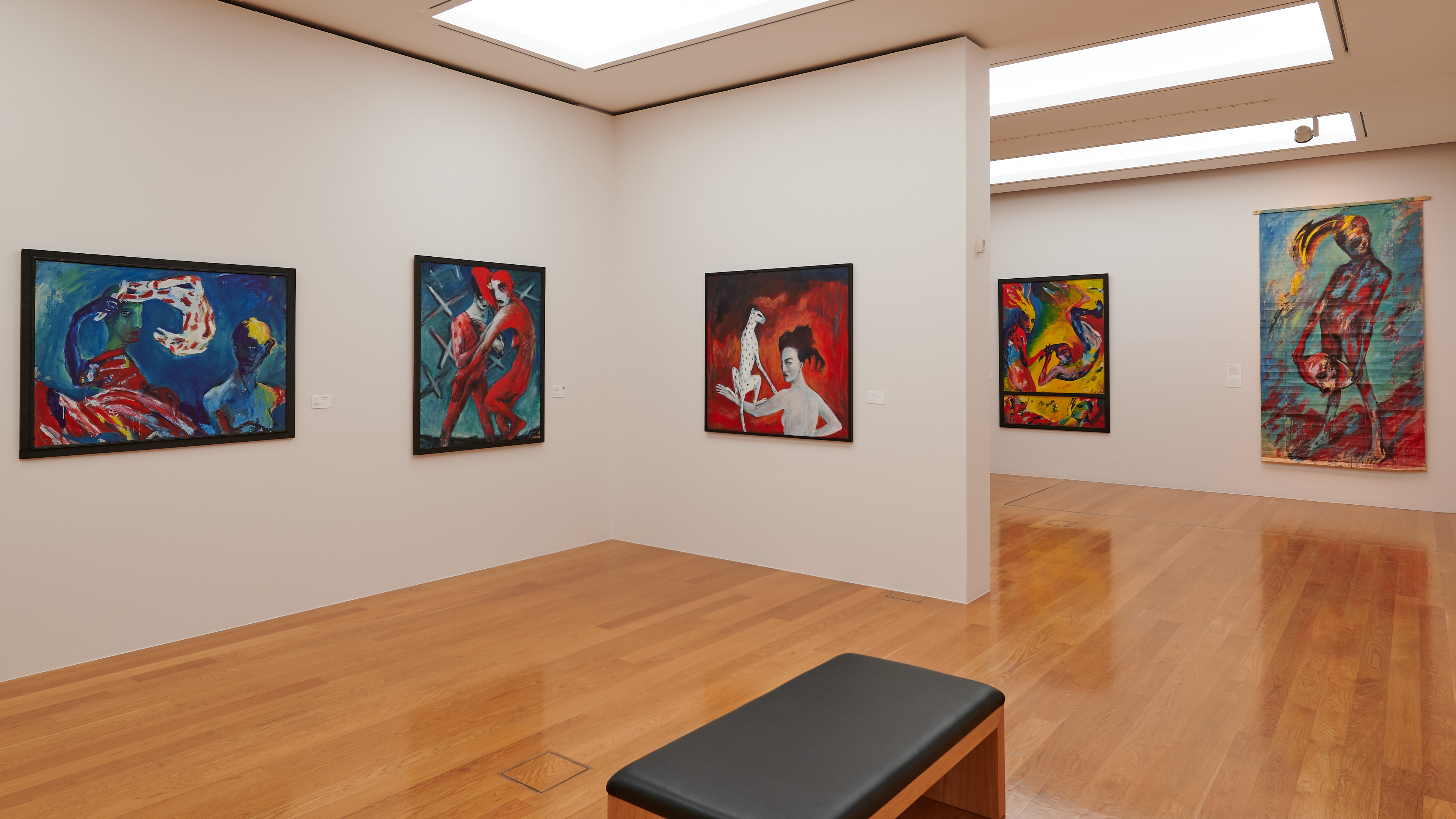 AI generated: The image shows a modern gallery space with several colourful paintings on the walls and a wooden floor. In the foreground is a black bench.