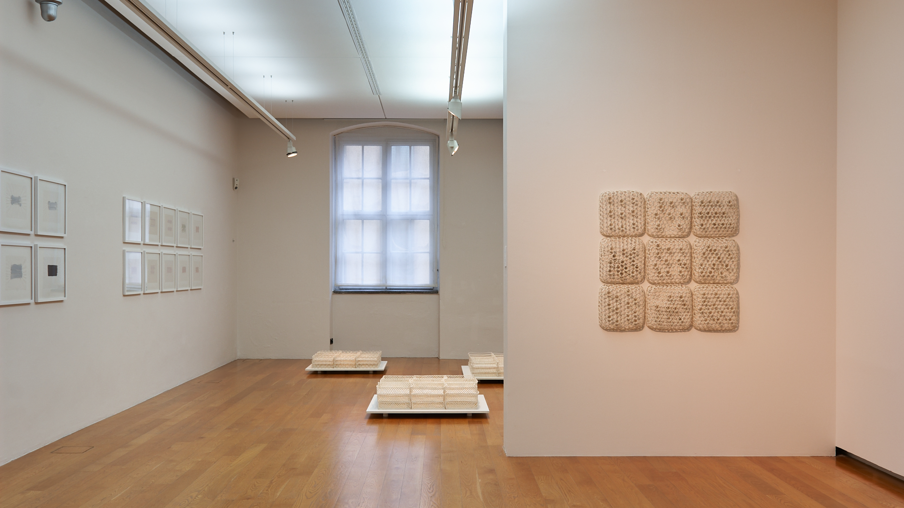 AI generated: The image shows a modern exhibition space with several works of art on the walls and on the floor, consisting of structured, square elements. The wooden floors and the minimalist design emphasise the works of art.