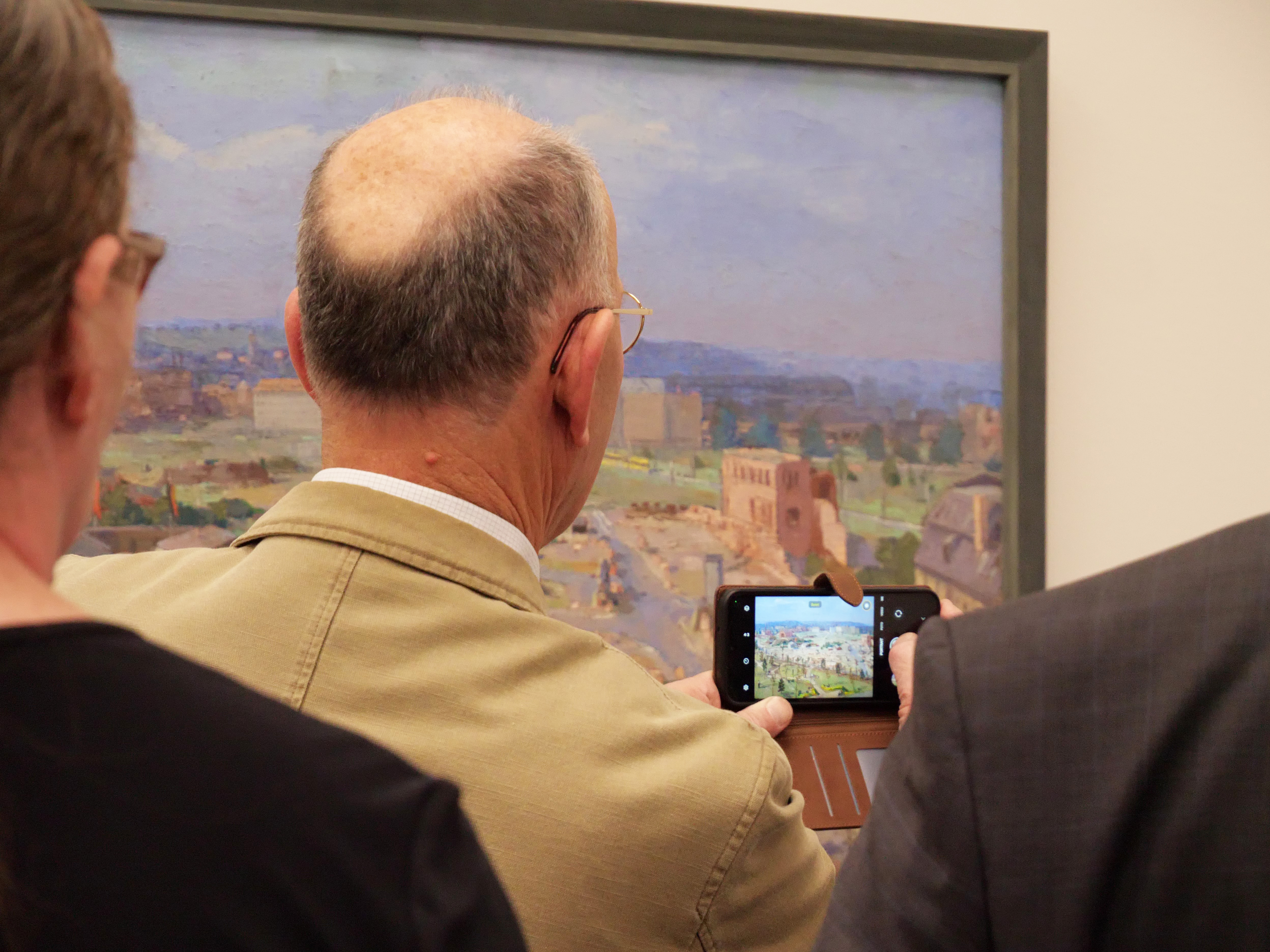 KI generiert: Ein Mann fotografiert ein Gemälde in einer Galerie mit seinem Smartphone. Das Bild zeigt den Moment, in dem er das Kunstwerk festhält.