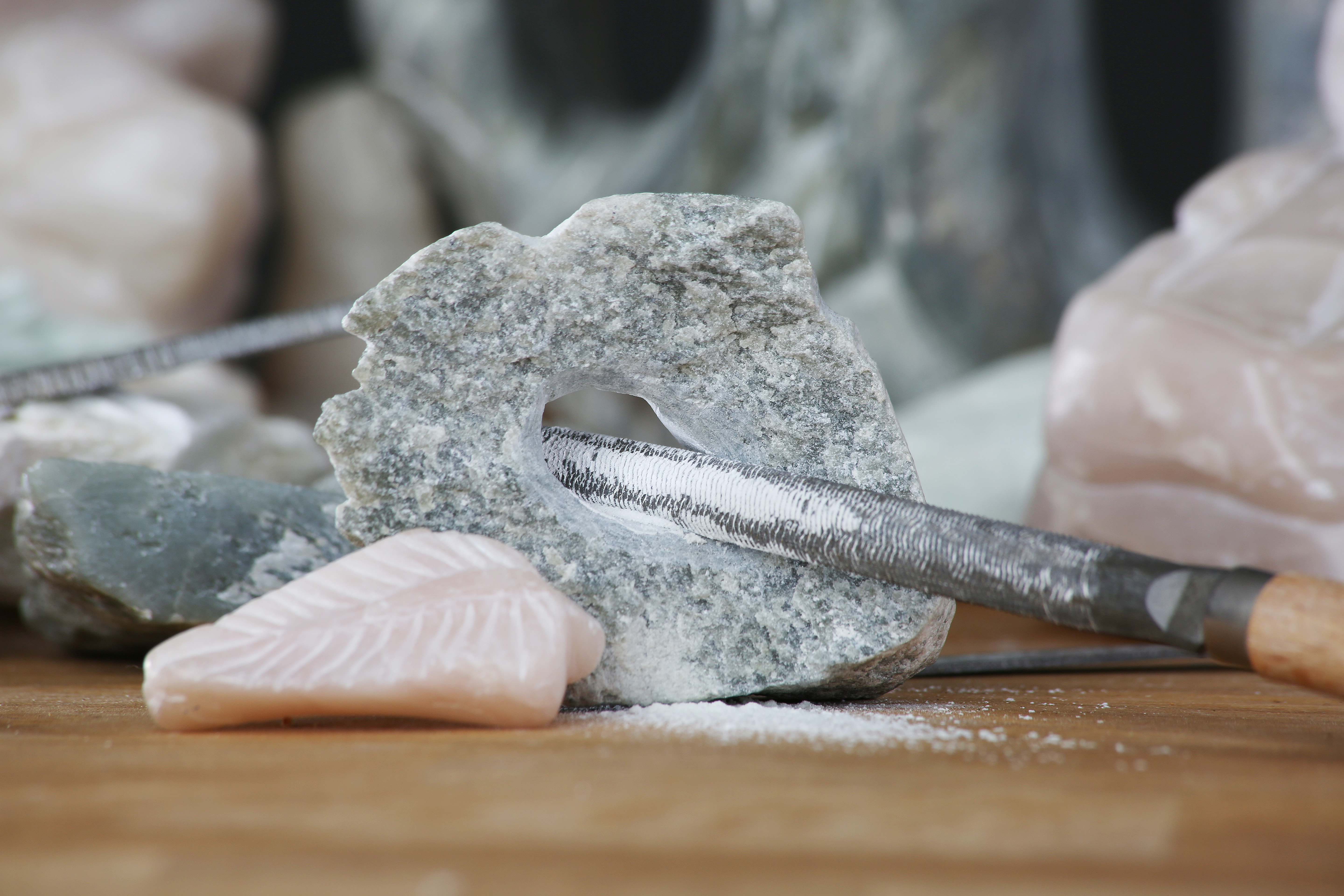 AI generated: The image shows a stone being worked with a file to form a hole. In the foreground, another tool and processed stone lie on a wooden surface.