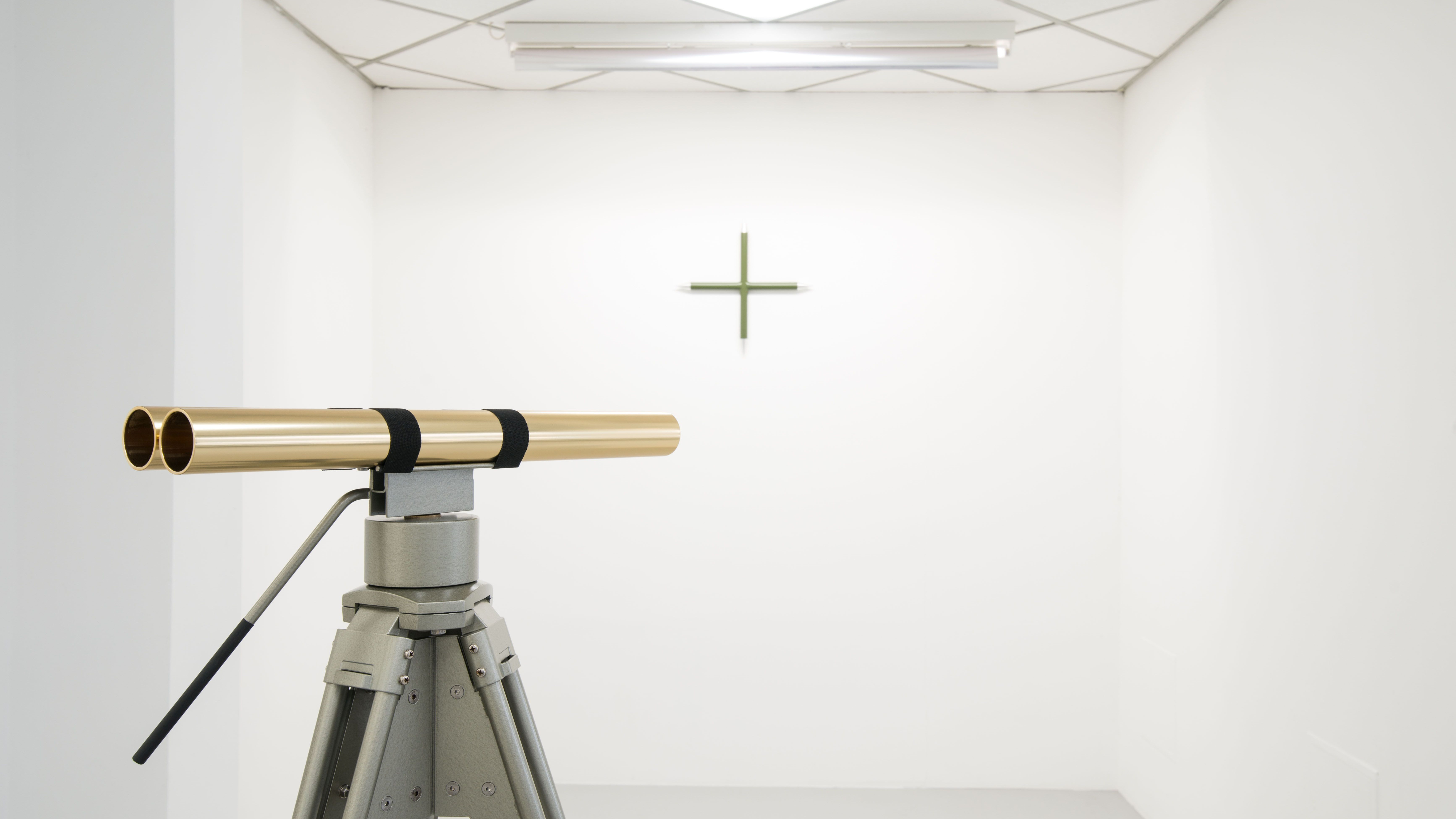 KI generiert: Das Bild zeigt eine Ausstellung mit einem goldenen Teleskop auf einem Stativ, das auf ein kleines Kreuz an der weißen Wand gerichtet ist. Die Szene wirkt minimalistisch und steril.