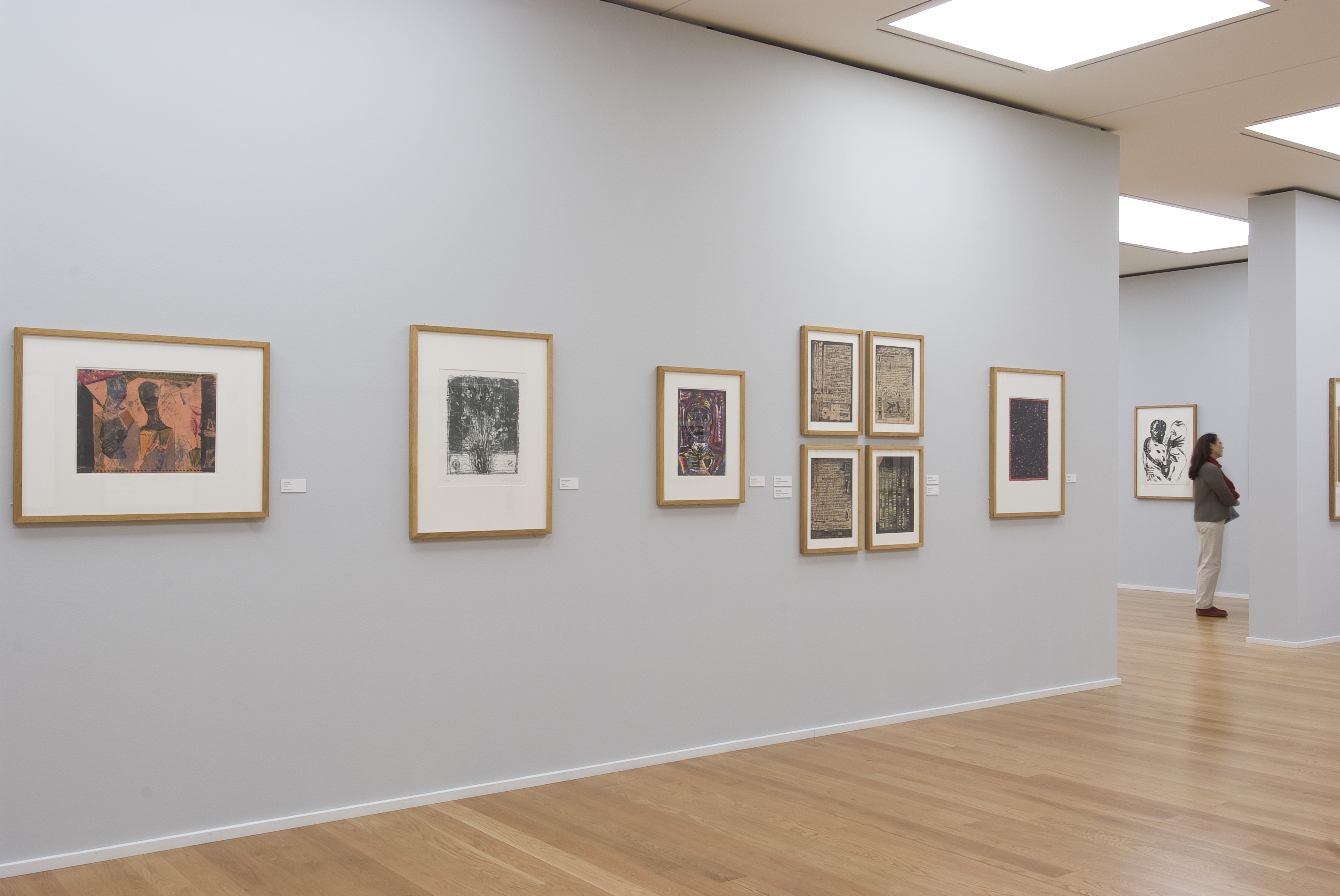 KI generiert: Das Bild zeigt eine Kunstgalerie mit mehreren gerahmten Kunstwerken an einer weißen Wand. Eine Person betrachtet die Kunstwerke, während sie in einem Raum mit Holzfußboden steht.