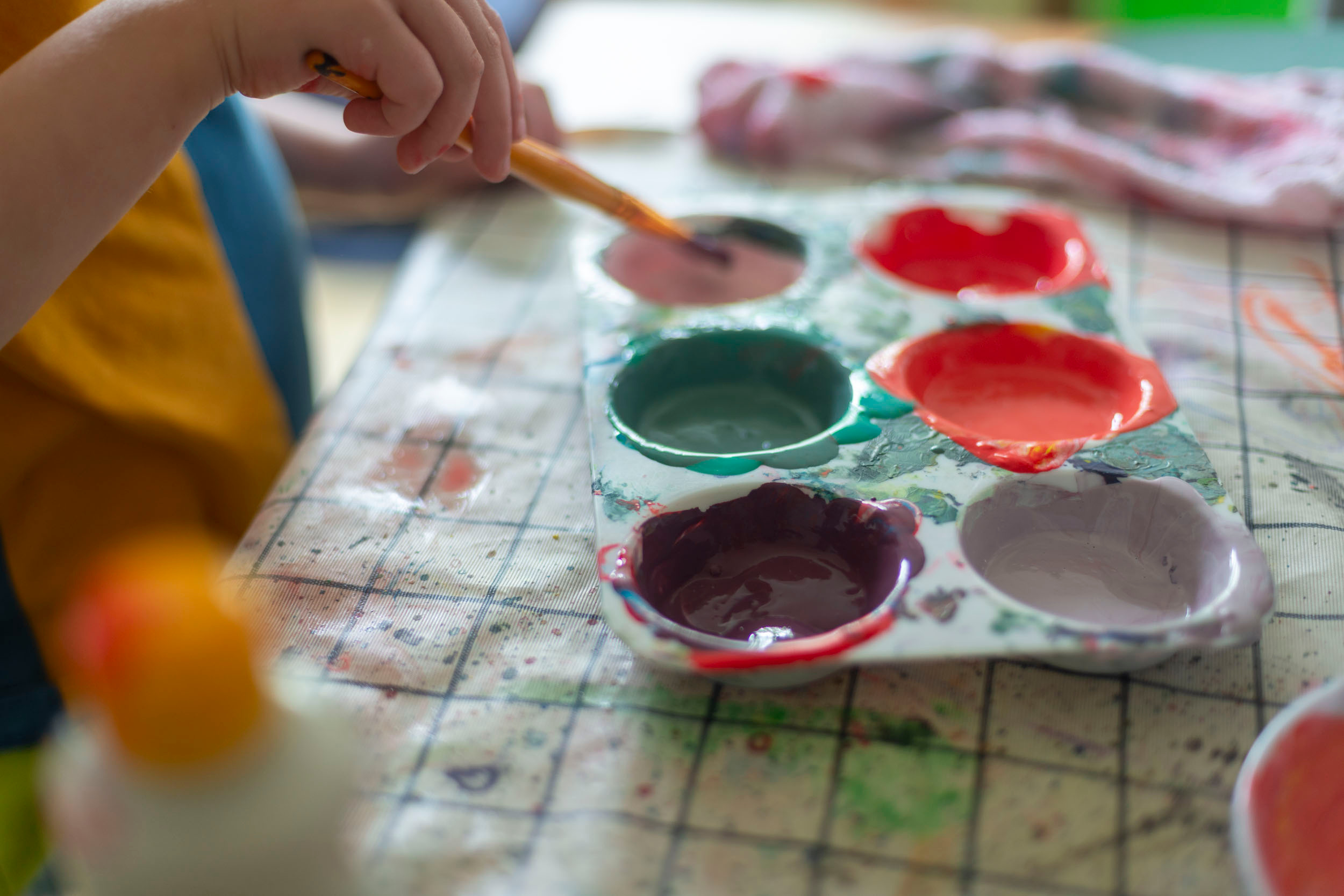 KI generiert: Ein Kind malt mit einem Pinsel und verwendet eine Palette mit verschiedenen Farben. Der Fokus liegt auf der kreativen Tätigkeit und der bunten Farbpalette.