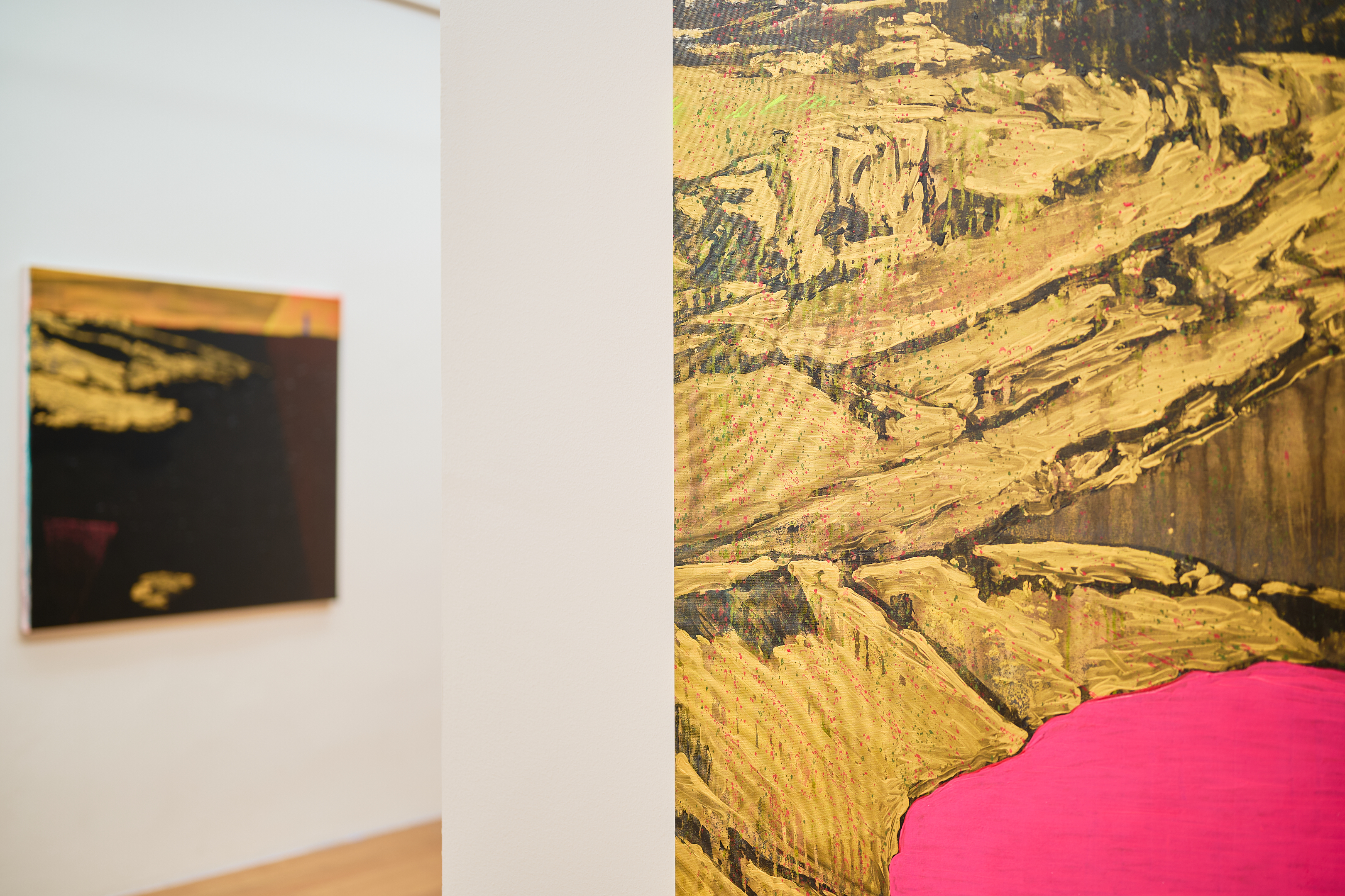 KI generiert: Das Bild zeigt eine Ausstellung mit zwei Gemälden, die abstrakte, goldene und rosa Farbtöne aufweisen. Der Fokus liegt auf dem vorderen Gemälde, während das hintere unscharf im Hintergrund erscheint.