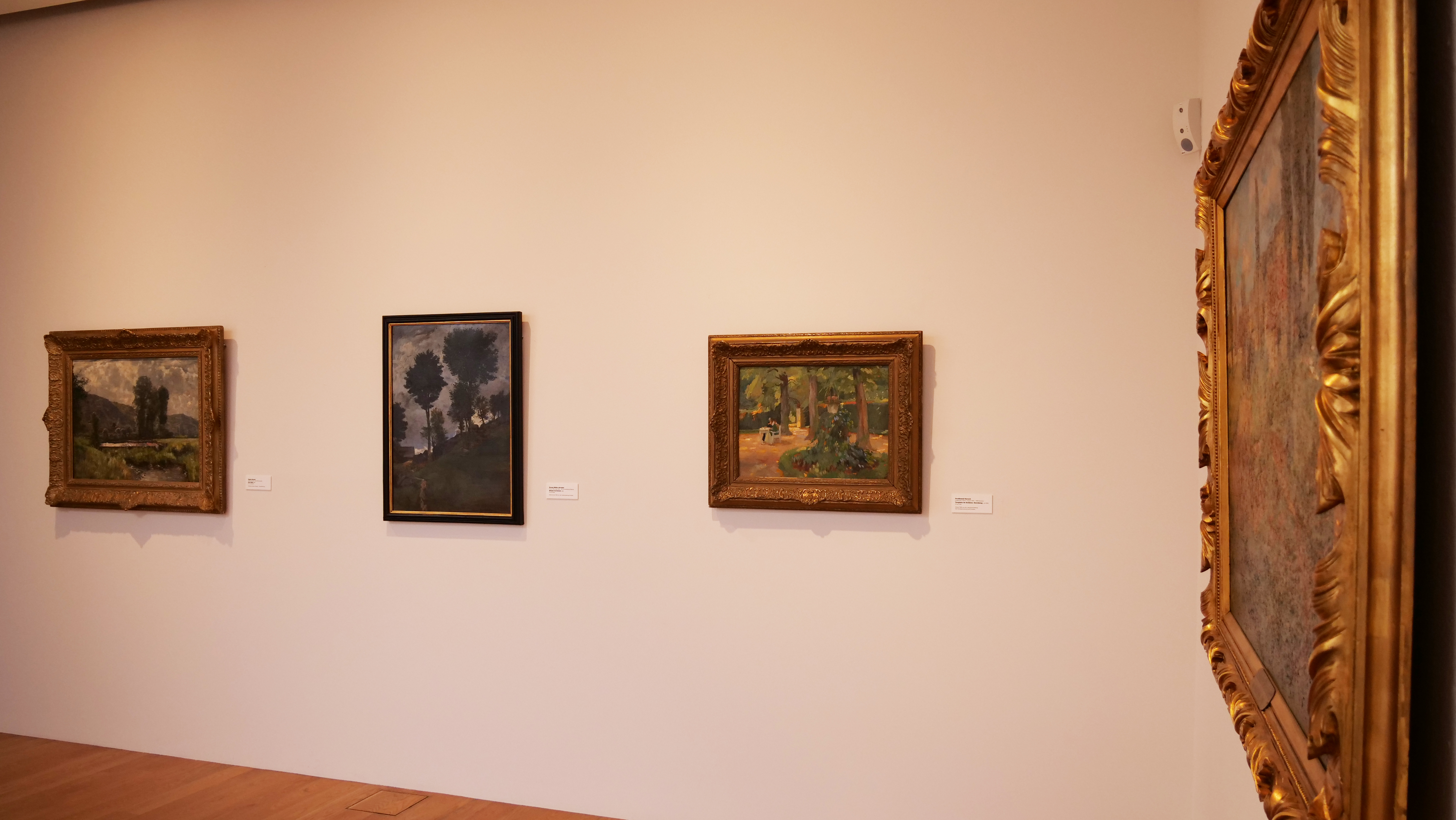 KI generiert: Das Bild zeigt eine Galerieausstellung mit mehreren gerahmten Gemälden an einer hellen Wand. Die Kunstwerke sind in klassischen Rahmen präsentiert und zeigen verschiedene Landschaftsszenen.