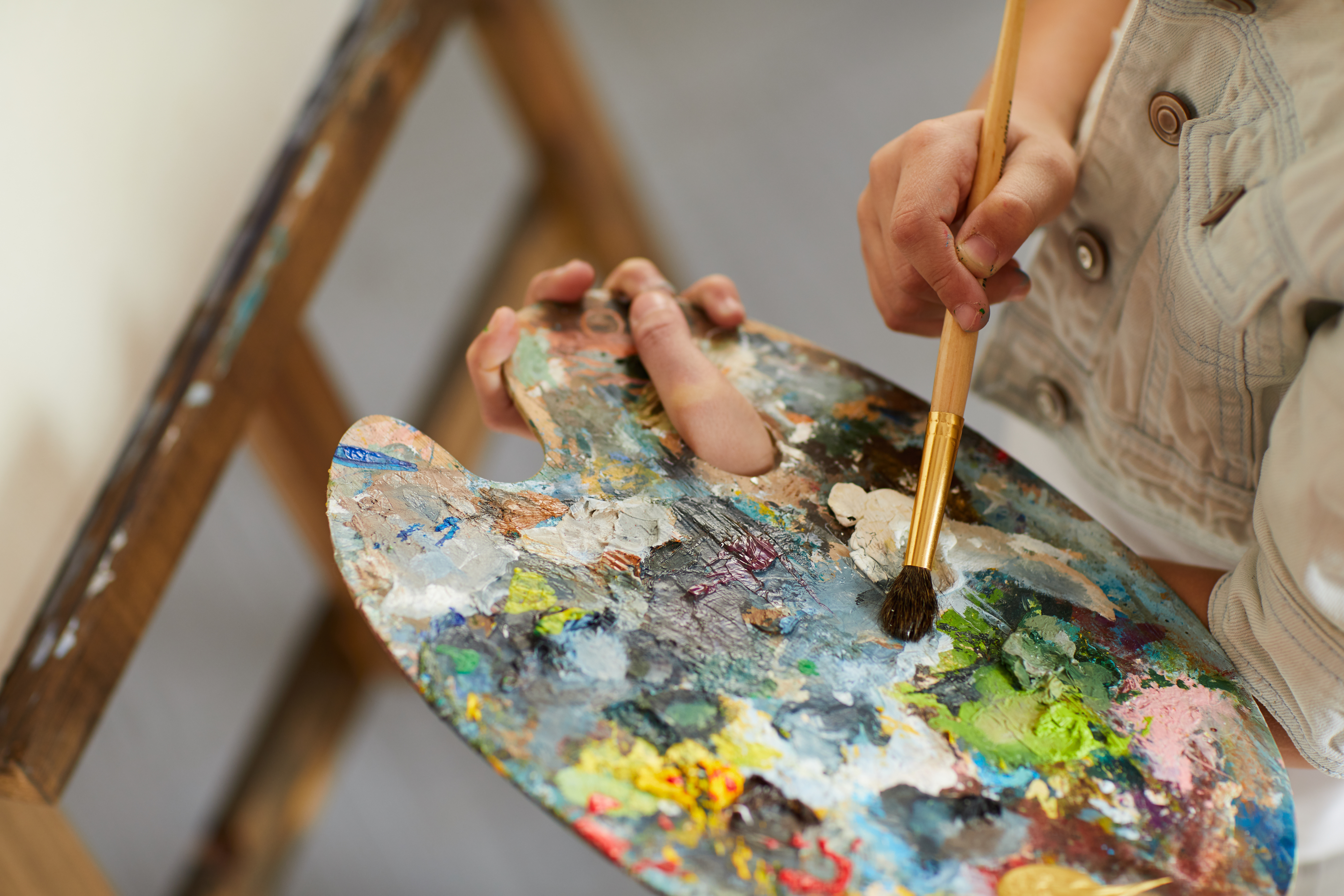 KI generiert: Das Bild zeigt eine Person, die eine Malpalette mit verschiedenen Farben in der einen Hand hält und mit der anderen Hand einen Pinsel benutzt. Der Fokus liegt auf der Malaktivität und den lebendigen Farben auf der Palette.