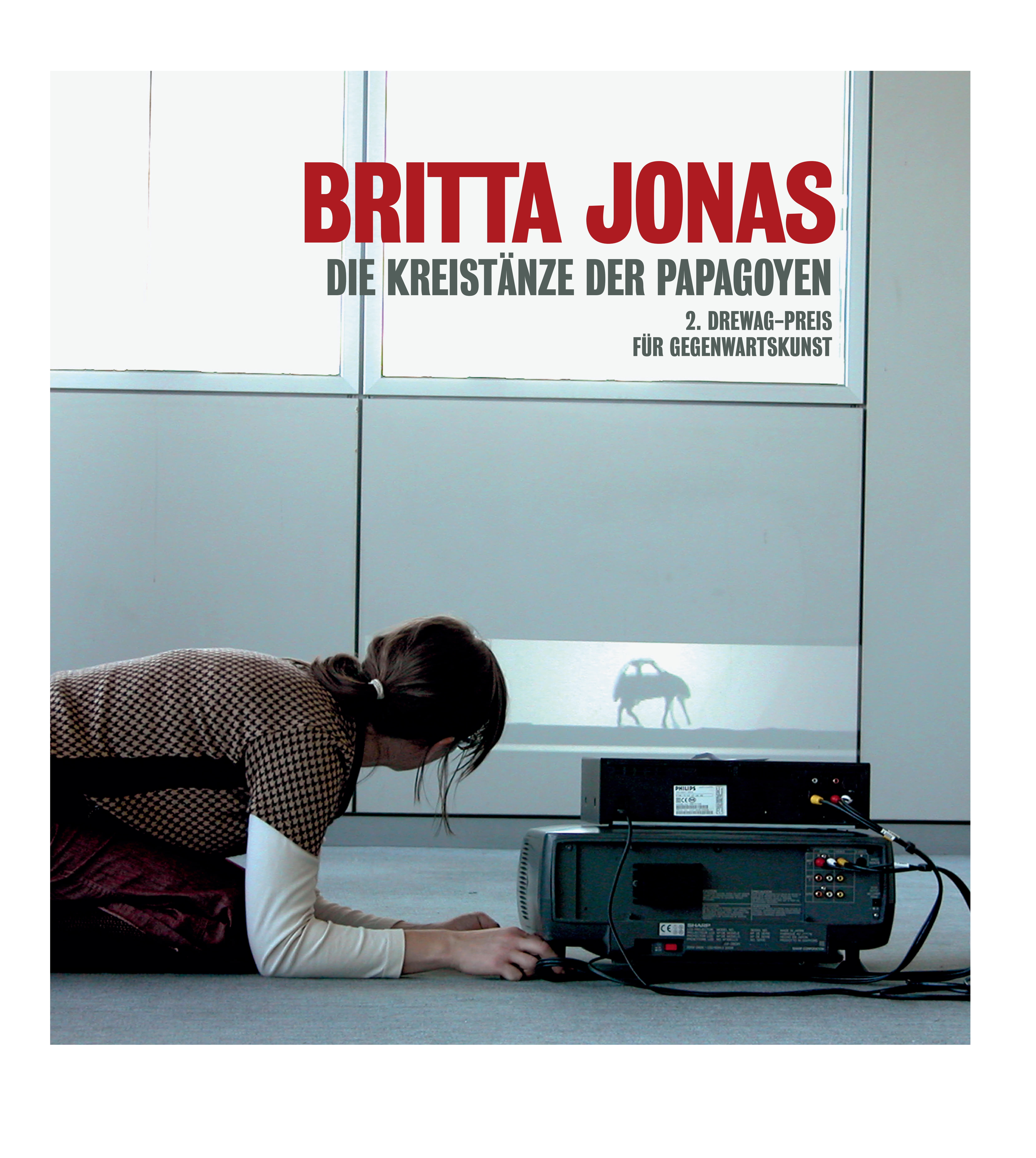KI generiert: Eine Person liegt neben einem Projektor, der ein Bild eines Kamels an eine Wand projiziert. Der Text "Britta Jonas: Die Kreistänze der Papageien" ist groß über dem Bild zu sehen.
