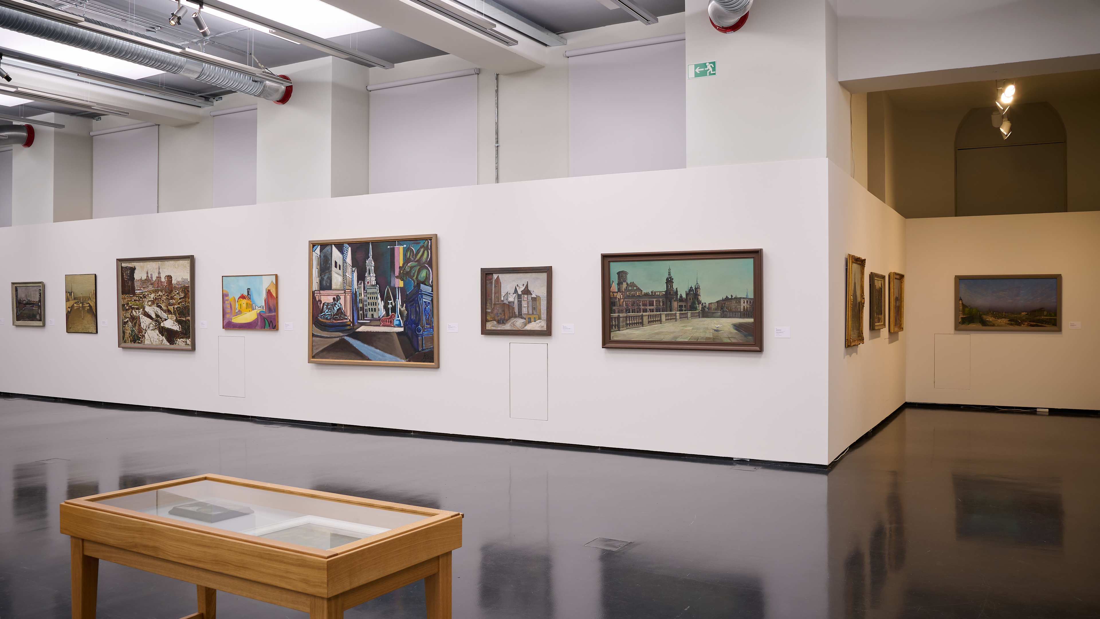 KI generiert: Das Bild zeigt eine Kunstgalerie mit mehreren Gemälden, die an den Wänden ausgestellt sind. Im Vordergrund befindet sich ein Glastisch, der möglicherweise weitere Ausstellungsstücke enthält.